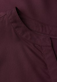 Burgunderfarbener Stoff mit glatter Textur, der einen runden Ausschnitt und subtile Stichdetails entlang der Kanten aufweist.