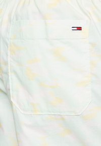 Primo piano di una tasca in tessuto tie-dye pastello con un piccolo logo di marca rettangolare rosso, bianco e nero nell'angolo in alto a destra.