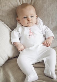 Body bianco in cotone con design di giraffa caratterizzato da macchie rosa e testo. Il design include un cappuccio e chiusure a scatto lungo le gambe.