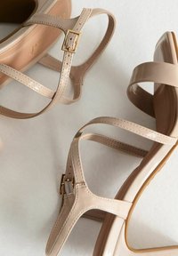 Beige sandalen met bandjes, gemaakt van glad synthetisch materiaal met een glanzende afwerking, met goudkleurige gespdetails en een gevormde zool.