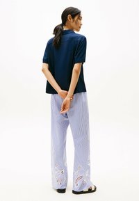 Camisa de manga corta azul marino con un corte relajado, combinada con pantalones a rayas azules que presentan detalles florales bordados en blanco en el dobladillo.