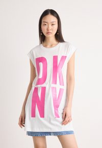 T-shirt bianco oversize con lettering rosa lucido "DKNY", con scollatura rotonda e maniche corte. Gonna di jeans visibile in basso.