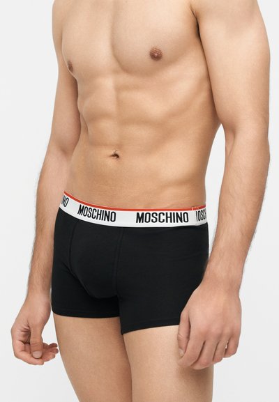 Αρσενικός κορμός που φοράει μαύρα μποξεράκια με λευκή μέση που φέρει το λογότυπο Moschino με μαύρα γράμματα.