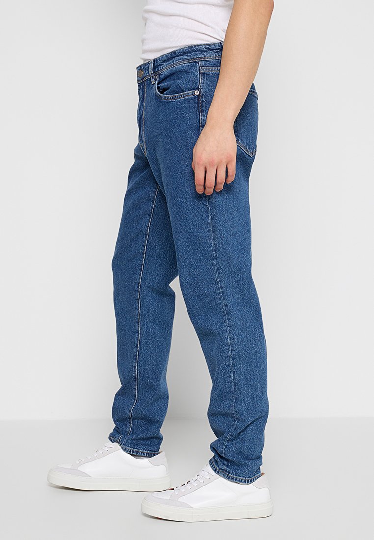 Blauwe denim jeans met een rechte pijp, vijf zakken en subtiele stiksels, gecombineerd met witte sneakers.