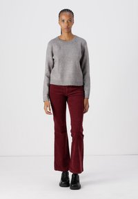 Suéter gris de punto con cuello redondo, combinado con pantalones acampanados de pana rojos y zapatos de plataforma negros, llevado por una persona de pie.