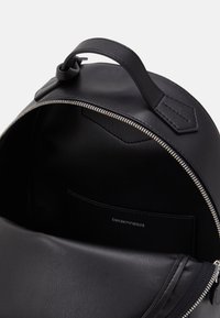 Round black leather backpack with a zip closure. Interior features a smooth finish and a small pocket displaying branding.