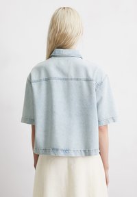 Light blue denim short-sleeve jacket with a collar, featuring a relaxed fit and visible stitching. Back view showcases a cropped design.