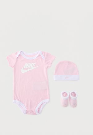Ensemble bébé Nike rose avec un body à manches courtes, un bonnet assorti et des chaussons, tous bordés de blanc.