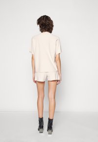 Haut en tricot beige à manches courtes et short assorti, offrant une coupe décontractée. Bottines noires à talons carrés.