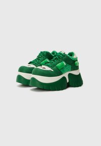 Sneaker piattaforme verdi con una combinazione di suede testurizzato e materiali simili alla pelliccia. Suola e lacci spessi, con un design che presenta accenti bianchi e verdi.