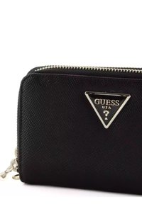 Portefeuille noir texturé avec fermeture éclair argentée, présentant un logo Guess en forme de triangle sur le devant. Forme rectangulaire compacte avec des accents lisses.