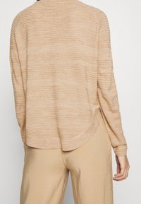 Ljus beige tröja med horisontell ribbad textur, avslappnad passform och sjunkna axlar, med rundad nederkant och långa ärmar.