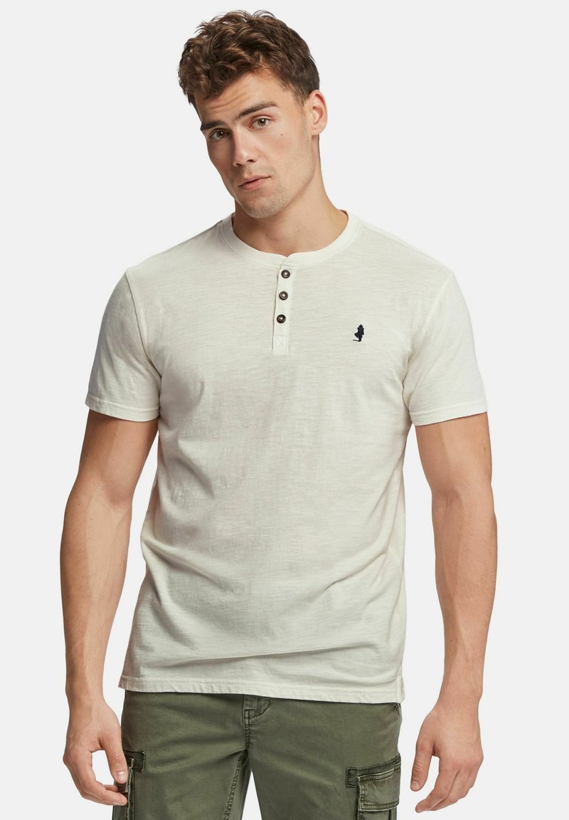 Gai beigā krāsā īsām piedurknēm henley krekls ar trim brūnām pogām uz apkakles; tam ir neliels tumši zils logo kreisajā krūšu pusē.