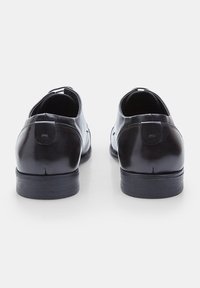 Scarpe da uomo in pelle nera con una superficie liscia, punta arrotondata e tacco basso impilato, con un delicato dettaglio di cucitura sul retro.