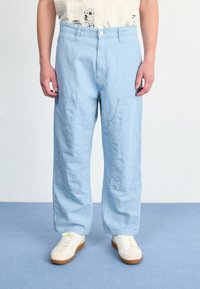 Lichtblauwe, loszittende broeken van zacht materiaal, met zijzakken en een knoopsluiting, gecombineerd met witte sneakers.