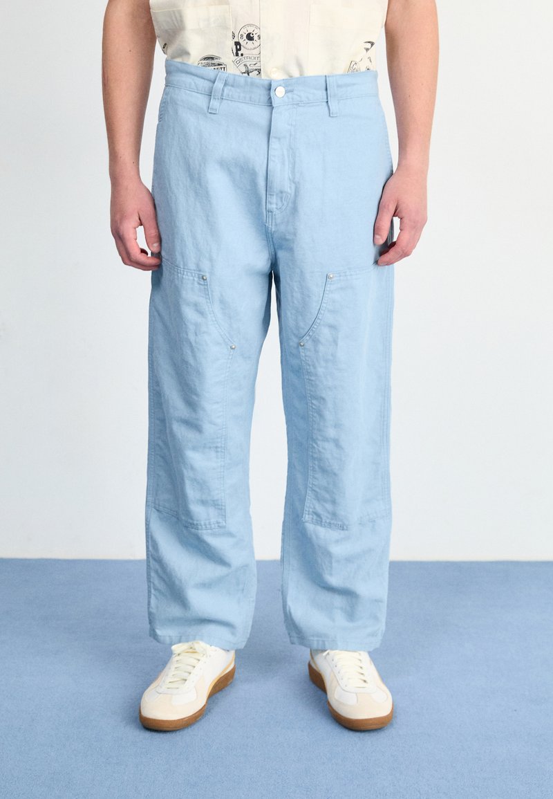 Lichtblauwe, loszittende broeken van zacht materiaal, met zijzakken en een knoopsluiting, gecombineerd met witte sneakers.