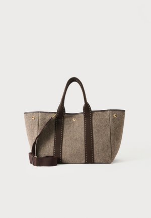 Bolsa tote de tela marrón con asas marrón oscuro y una correa de hombro ajustable sobre un fondo blanco.