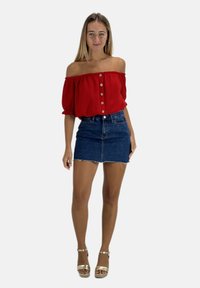 Rode off-shoulder top met knoopdetails, gecombineerd met een denim minirok. Doorzichtige stof, losse pasvorm en gestructureerde afwerking, aangevuld met gouden schoenen.