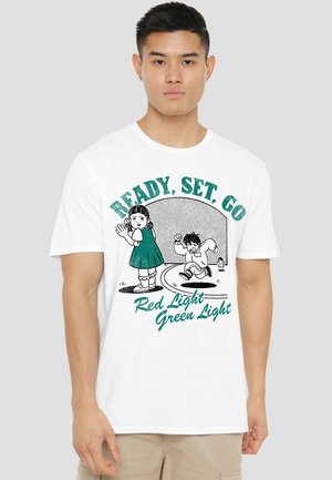 White cotton t-shirt featuring a graphic design of children playing with the text "READY, SET, GO" and "Red Light Green Light" in green.