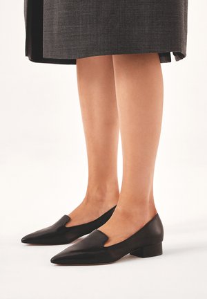 Scarpe in pelle nera con punta appuntita e design a intaglio, caratterizzate da un tacco basso a blocco e una texture liscia.