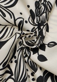 Tessuto floreale nero con sfondo crema, caratterizzato da audaci motivi astratti di foglie e petali. Texture liscia e caduta morbida.