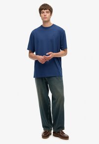 Camiseta de algodón azul marino con cuello redondo, corte holgado, combinada con vaqueros de mezclilla azul oscuro de corte ancho y zapatos marrones con cordones.