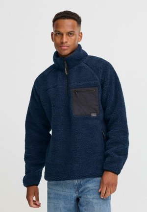 Navy fleece pullover with a half-zip collar, featuring a black zippered chest pocket and textured fabric, designed for warmth and comfort.