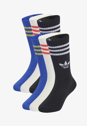 Fem par midt-på-lægs Adidas-strømper i sort med hvide striber og logo, hvide med røde striber og blå med gule striber, placeret side om side.