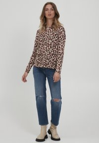 Dlouhý rukáv s krémovým základem a maroon a hnědým leopardím vzorem; spárováno s roztrhanými modrými džíny a béžovými kotníkovými botami.