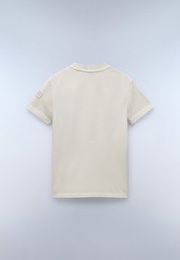 T-shirt beige a maniche corte con collo rotondo classico, caratterizzato da un tessuto testurizzato e una piccola toppa decorativa sulla manica sinistra.