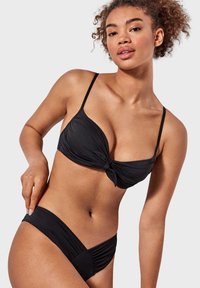 Conjunto de bikini negro que incluye una bralette anudada con tirantes finos y braguitas de tiro bajo con fruncidos. Tela suave y elástica con un acabado mate.