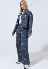 Takkihousu ja leveät farkut, tummansininen, valkoisella nauha-enkeliompeluksella, jossa on napit ja taskut, yhdistettynä valkoisiin tennareihin.