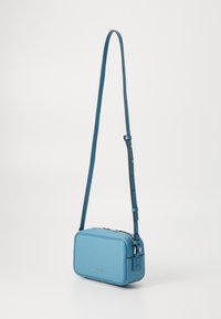 Geantă crossbody din piele de culoare bleu deschis, cu formă rectangulară, suprafață texturată, curea ajustabilă și închidere cu fermoar argintiu.