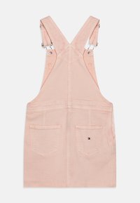 Vestido de tirantes de mezclilla rosa con tirantes ajustables, detalles cosidos y dos bolsillos traseros. Pequeño parche con el logo ubicado encima del bolsillo derecho.