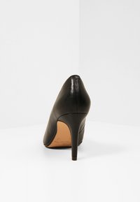 Scarpa nera in pelle con tacco alto, punta affusolata e tacco sottile e affusolato. Texture liscia e design minimalista senza hardware visibile.