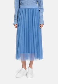 Gonna in tulle azzurro chiaro con design plissettato, vita elastica e lunghezza completa, abbinata a sneakers bianche, per un look stratificato e arioso.