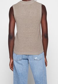 Haut beige sans manches en tricot à texture côtelée avec un col arrondi, associé à un jean denim bleu clair avec des accents usés.