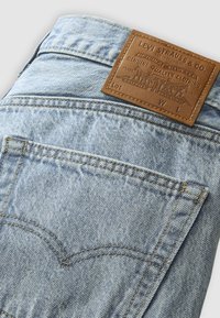 Jasnoniebieskie dżinsy z denimu z widoczną tylną kieszenią oraz brązową skórzaną metką marki Levi Strauss & Co. z przeszyciami.