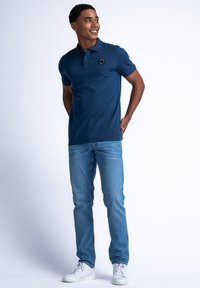 Námořnická polo tričko s krátkými rukávy a límečkem, se malým černým logem. V kombinaci se světlými modrými džíny a bílými teniskami.