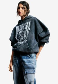 Bluza z kapturem w wyblakłym czarnym kolorze z białym graficznym logo i kwiatowym wzorem. Połączona z jasnoniebieskim denimem, posiadającym kieszenie typu cargo.