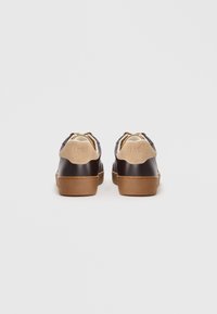 Pair of dark brown leather sneakers with beige suede heel tabs and brown rubber soles, viewed from the back on a white background.