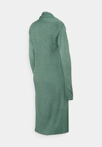 Cardigã de mangas compridas, até aos joelhos, em tecido de malha texturada verde. Apresenta um decote alargado e fendas laterais para facilitar o movimento.