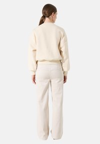 Sudadera crema con hombros caídos, combinada con pantalones de pierna ancha en un suave tono beige claro. Ambos confeccionados con tejidos suaves y texturizados.