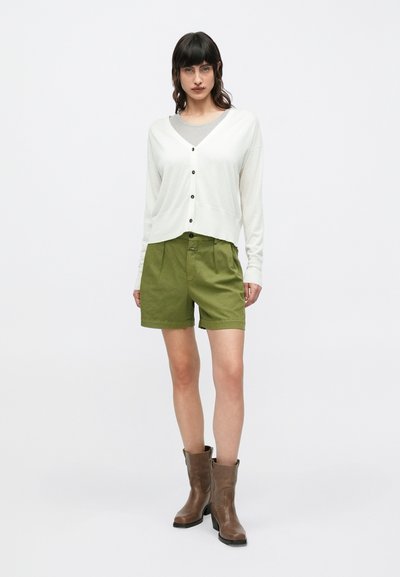 Λευκό μπλουζάκι με μακριά μανίκια και κουμπιά, πράσινο σορτς με ψηλή μέση και καφέ μποτάκια αστραγάλου. Απλός σχεδιασμός με χαλαρή εφαρμογή.