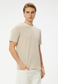 Camiseta de manga corta a rayas en crema y beige, con cuello redondo y un corte relajado. Hecha de tela ligera.