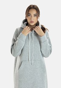 Sudadera con capucha gris de corte holgado, que cuenta con un bolsillo frontal y cordones blancos, confeccionada en un tejido suave y texturizado.