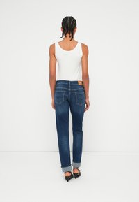 Jeans classici in denim blu con gamba dritta e orli rialzati, presentati con una canotta bianca semplice e tasche posteriori minimaliste.
