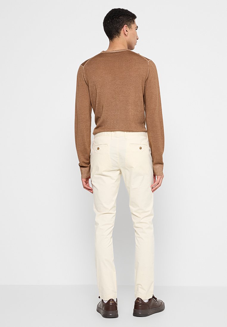 Pull en maille marron, chinos beiges et chaussures marron. Le pull a un design ajusté, les chinos ont une coupe droite avec des poches et des détails en bouton.