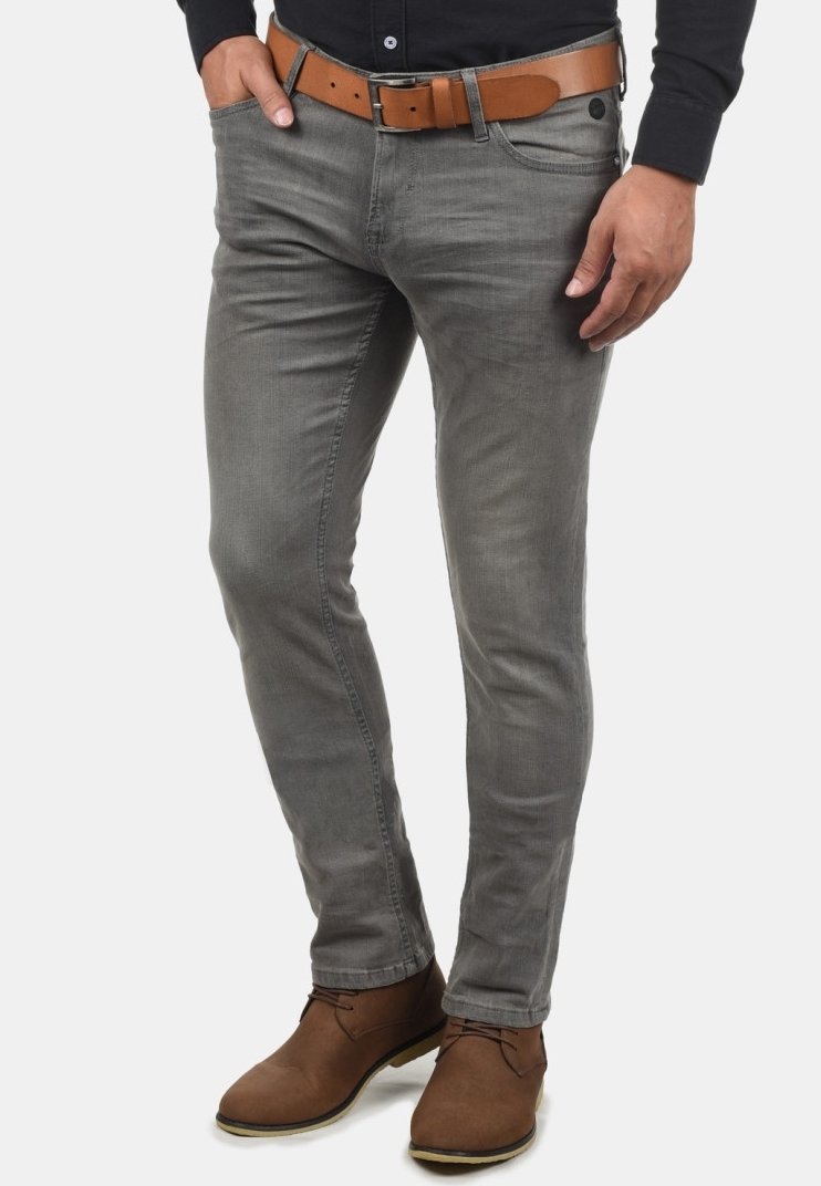 Homme portant un jean gris slim avec une ceinture marron et des chaussures marron à lacets assorties, debout avec une main dans la poche.