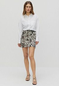 Hvid langærmet skjorte med krave parret med en tætsiddende leopardmønster mini nederdel. Sorte sandaler med stropper fuldender outfittet.